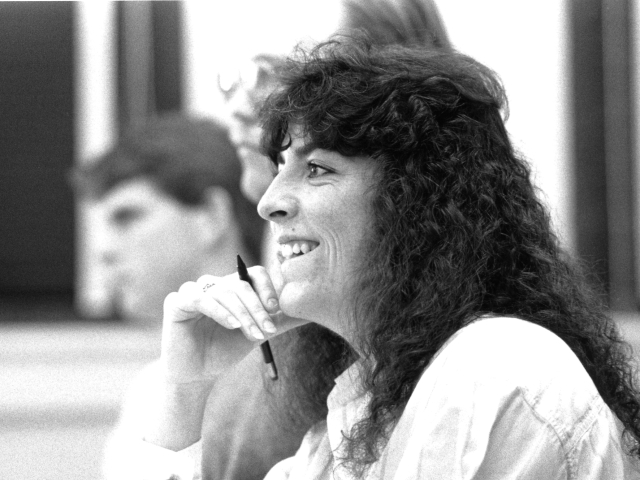 Black and white photo of a woman with curly hair holding a pencil