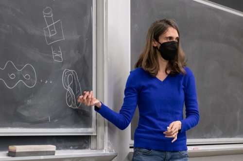 Member of Math Club at UC Davis points to equations drawn on a black board with white chalk.