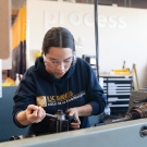 Student with UC Davis College of Engineering sweater works on a machine indoors